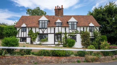 A traditional timber-frame house with white infill panels, a red tiled roof, and a brick chimney stack